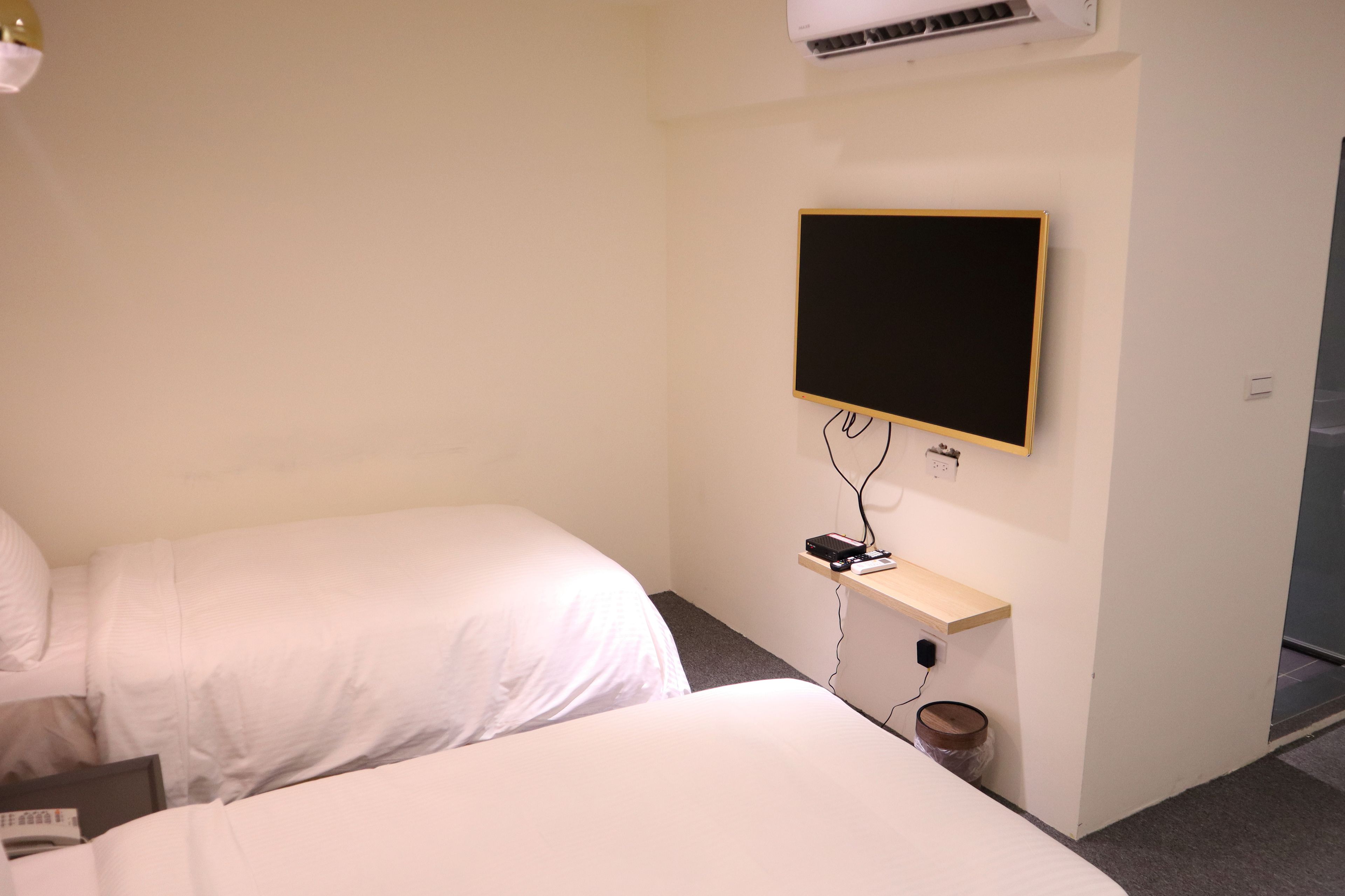 Ein Hotelzimmer mit zwei Betten, einem an der Wand befestigten Fernseher und einem kleinen Regal mit Telefon und Steckdose.