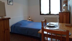 A small, well-lit room with a bed, a table with chairs, a window with curtains, a radiator, and a wooden cabinet. - Studio 2 people with parking Annecy (Annecy)