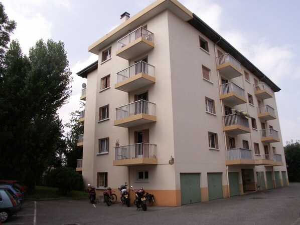 A multi-story residential building with balconies, a parking area, and a few parked motorcycles.