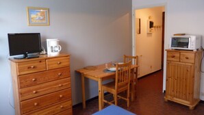 A small room with a wooden dresser, a television, a microwave, and a dining table with chairs. - Studio 2 people with parking Annecy (Annecy)