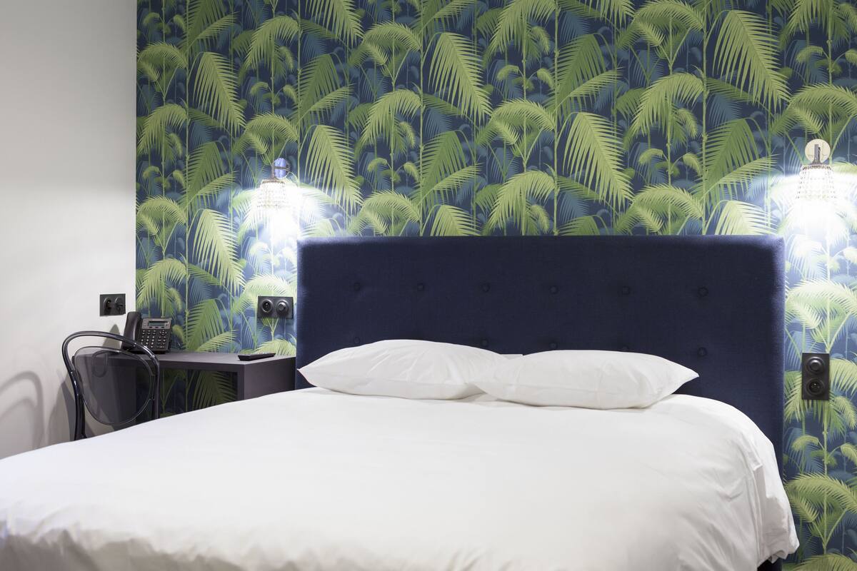 A hotel room with a bed, a desk with a phone, and a chair.