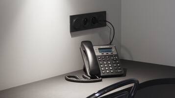Ett skrivbord med en telefon, en grenuttag och en vägglampa.