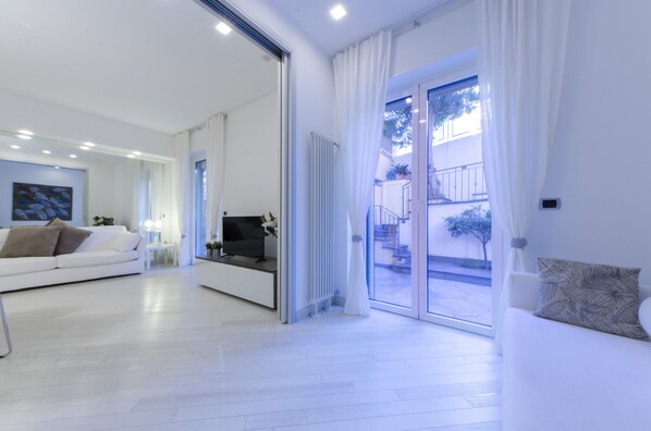 A modern living room with a sofa, TV, and a sliding glass door leading to an outdoor area.