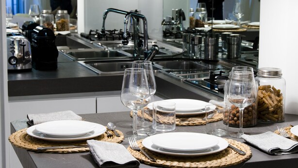 A modern kitchen with stainless steel appliances, a sink, and a dining area set with plates, glasses, and utensils. - JOIVY Nervi Charming Flat Santarosa (Genoa)
