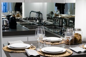 A modern kitchen with stainless steel appliances, a sink, and a dining area set with plates, glasses, and utensils. - JOIVY Nervi Charming Flat Santarosa (Genoa)