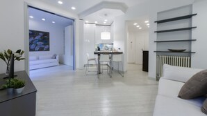A modern living room with a sofa, a dining area with a table and chairs, and a kitchen in the background. - JOIVY Nervi Charming Flat Santarosa (Genoa)