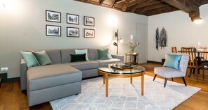A modern living room with a grey sectional sofa, a glass coffee table, and a patterned armchair. - JOIVY 9 Montenapo (Milan)