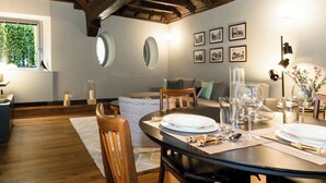 Un coin repas avec une table en bois dressée pour quatre personnes, un canapé et une fenêtre donnant sur un paysage verdoyant.