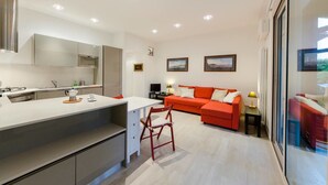A modern kitchen with a central island, a dining area with a red sofa, and a large window providing a view. - JOIVY Golf Garlenda - Charming Villa Guest House (Garlenda)