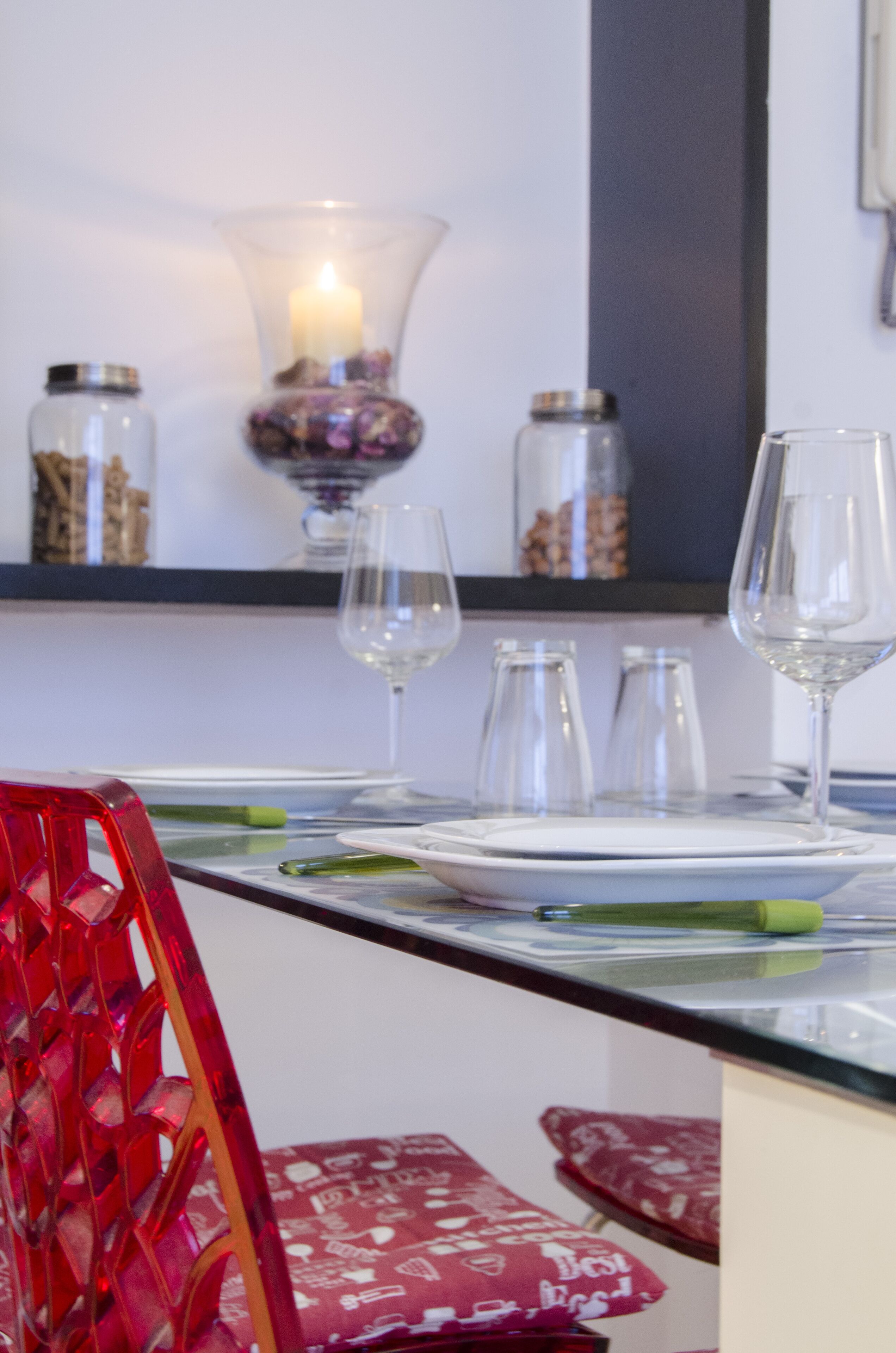 Een eettafel gedekt met transparant glaswerk, een kaars en decoratieve potten.