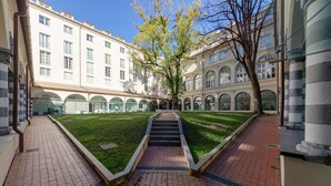 Une cour intérieure avec un escalier central, entourée de bâtiments dotés de fenêtres en arc et d’une pelouse.