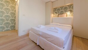 Une chambre à coucher avec un lit, une tête de lit dotée d’un éclairage intégré et un papier peint à motifs.