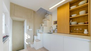 Une cuisine compacte avec des meubles blancs, une étagère en bois et un évier encastré.