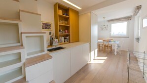 Une cuisine moderne dotée d’un îlot central intégré, d’un escalier en bois et d’un coin repas baigné de lumière naturelle.
