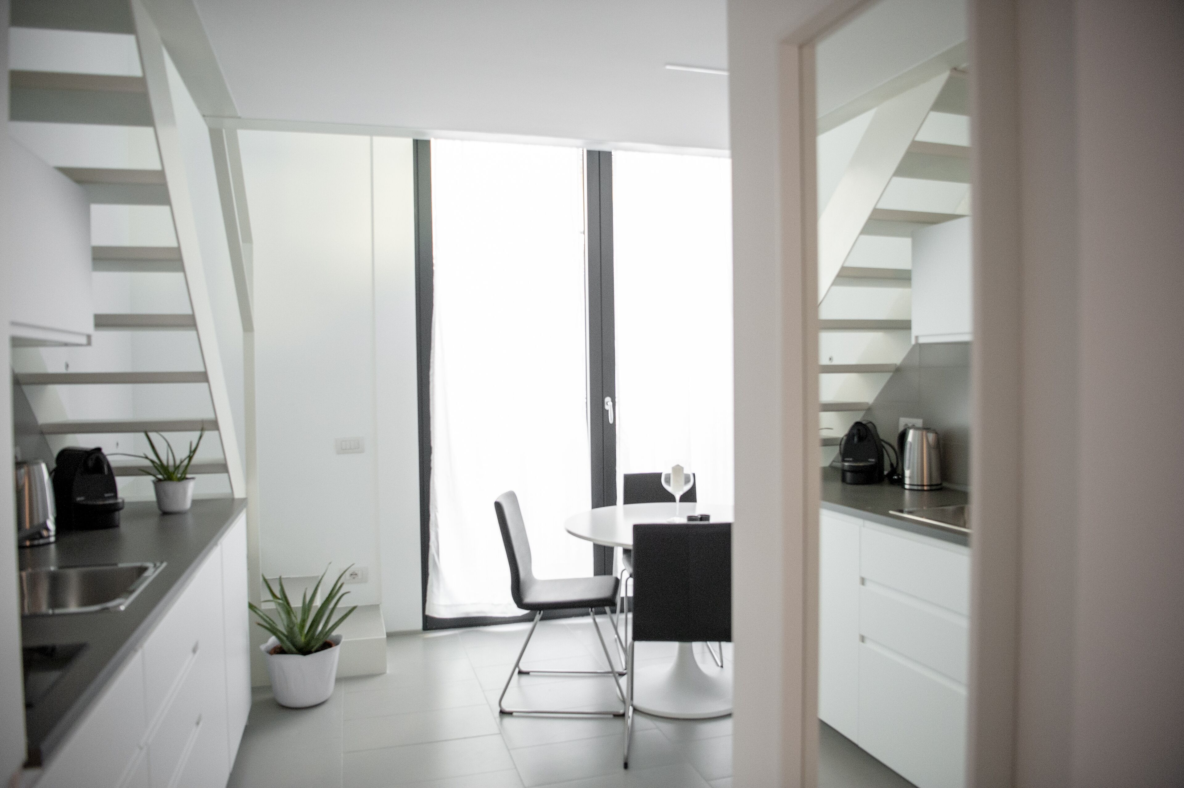 Een moderne keuken met witte kastjes, een eettafel met stoelen en een trap naar een hoger niveau.