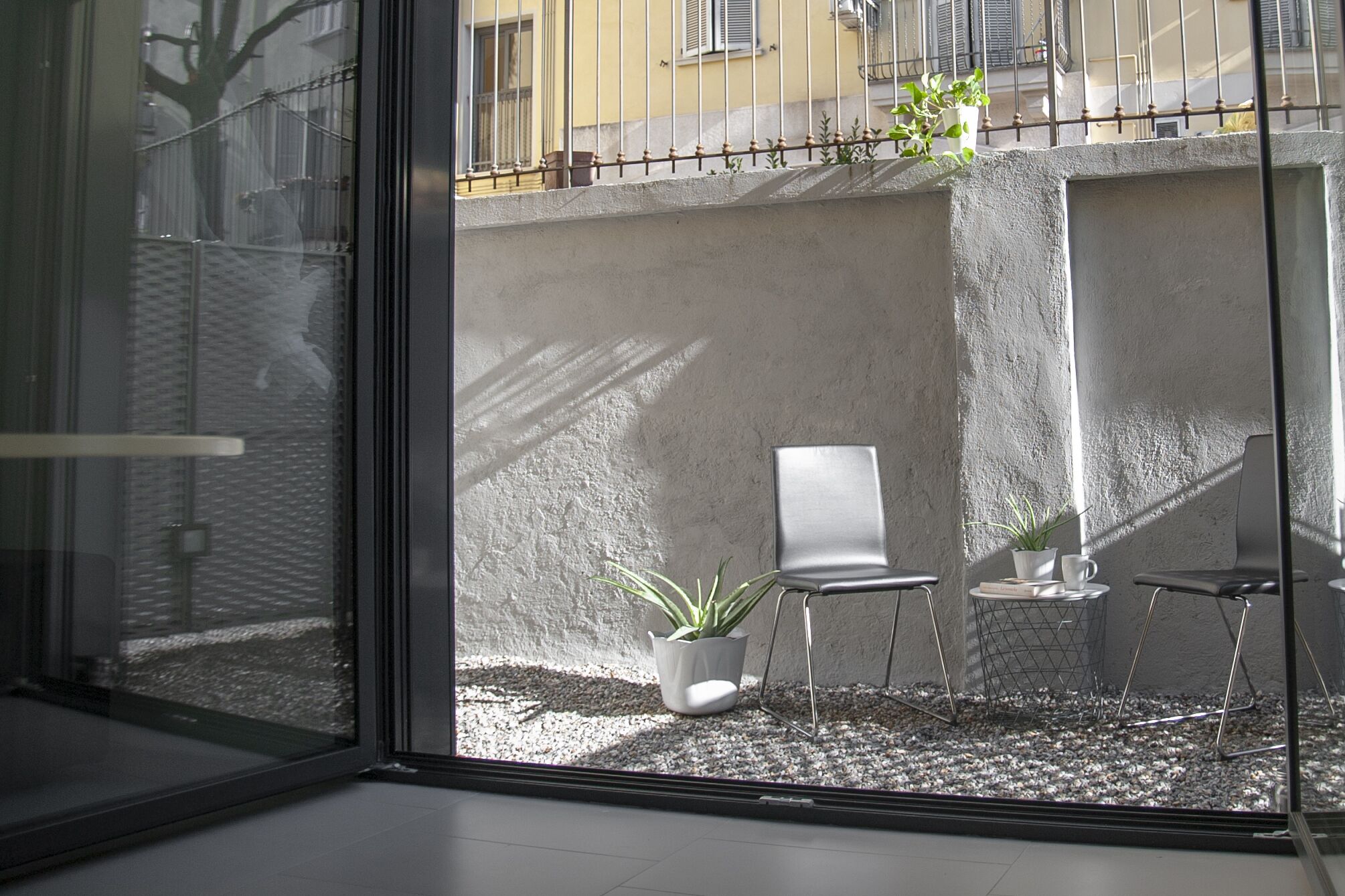 Un interior moderno con un separador de vidrio, una zona de estar con una silla y una mesita, y una planta en maceta.