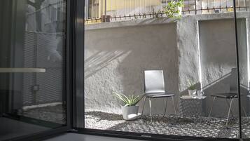 Un interior moderno con un separador de vidrio, una zona de estar con una silla y una mesita, y una planta en maceta.