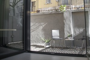 Een modern interieur met een glazen scheidingswand, een zithoek met een stoel en een klein tafeltje, en een potplant.
