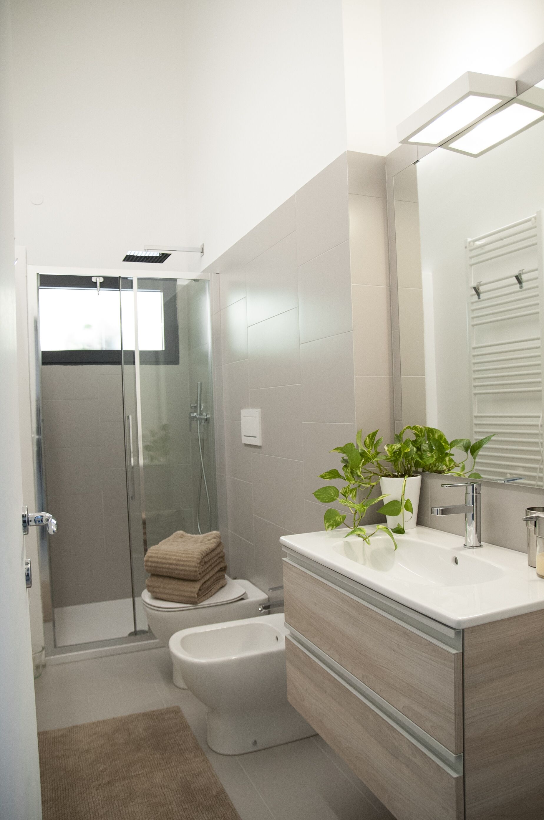 Un bany modern amb dutxa amb envàs de vidre, vàter, bidet i un moble de tocador amb mirall.