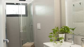 Un bany modern amb dutxa amb envàs de vidre, vàter, bidet i un moble de tocador amb mirall.