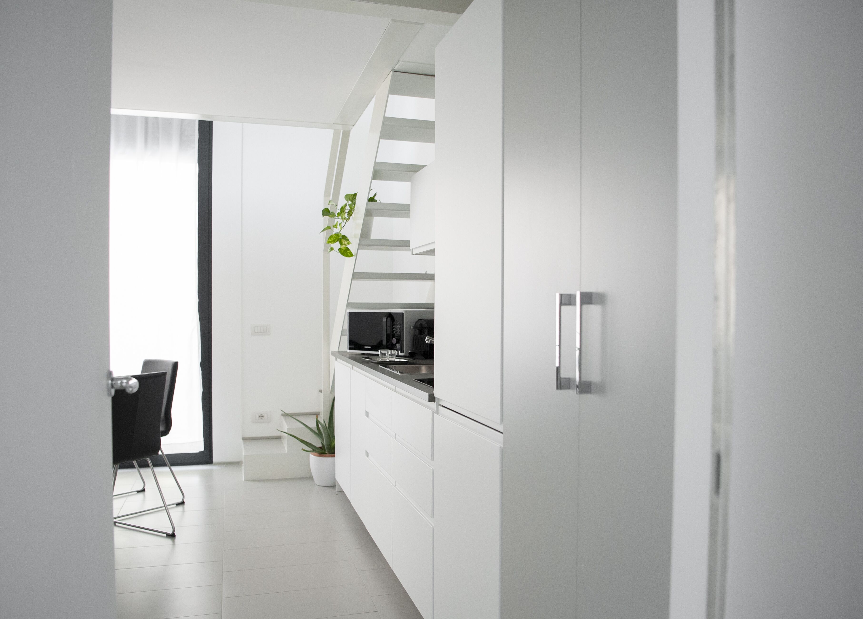 Una cocina moderna con armarios blancos, microondas integrado y un lavamanos de acero inoxidable.