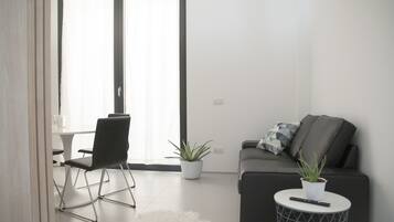 Una sala de estar moderna con un sofá, un sillón, una mesita redonda con un control remoto y una planta en maceta.