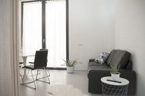 Een moderne woonkamer met een bank, een fauteuil, een klein rond tafeltje met een afstandsbediening en een potplant.