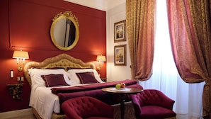 A hotel room with a large bed, two armchairs, a small table with apples, and a mirror on the wall.
