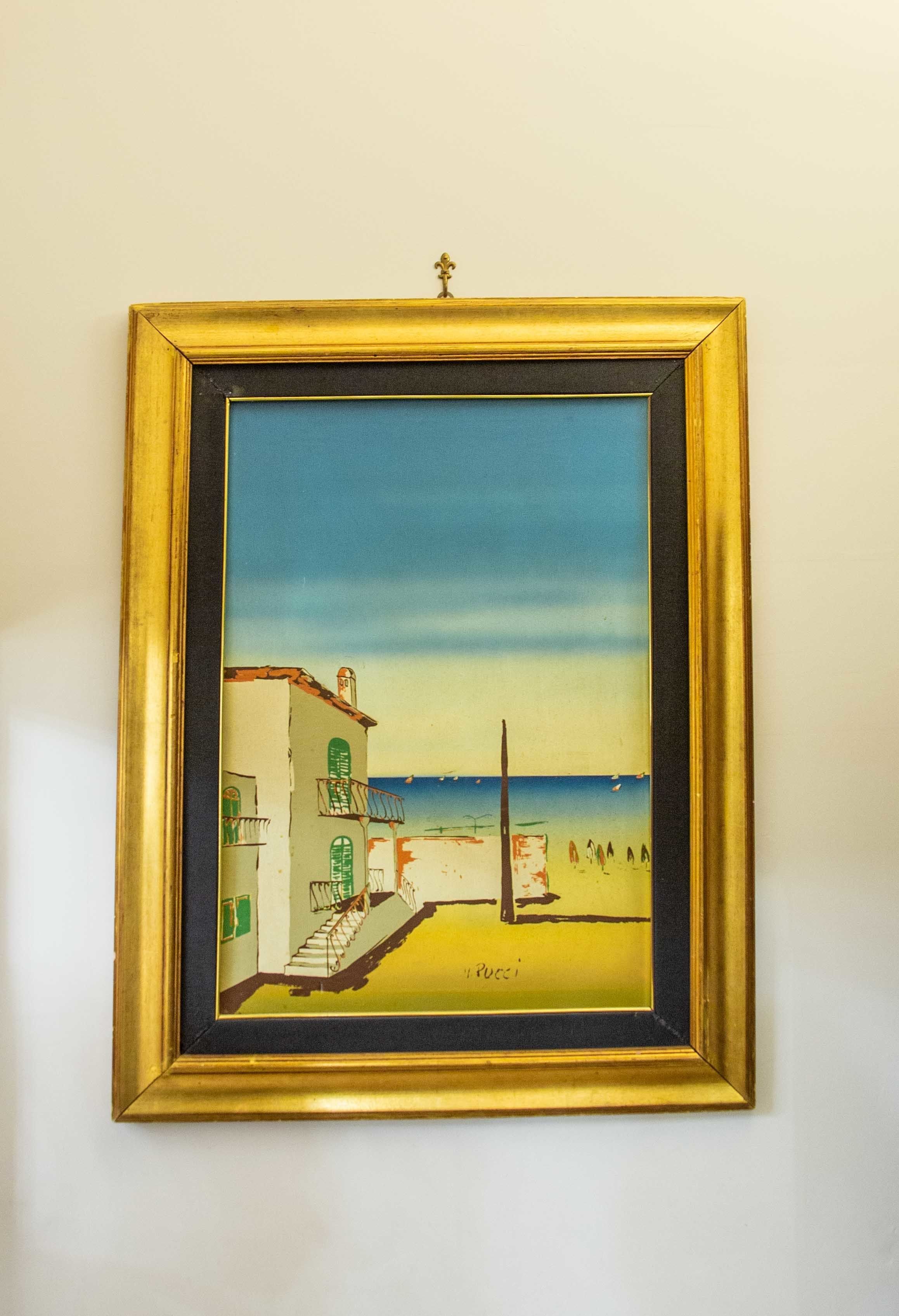 Un cuadro enmarco que muestra una escena costera con edificios y un muelle.