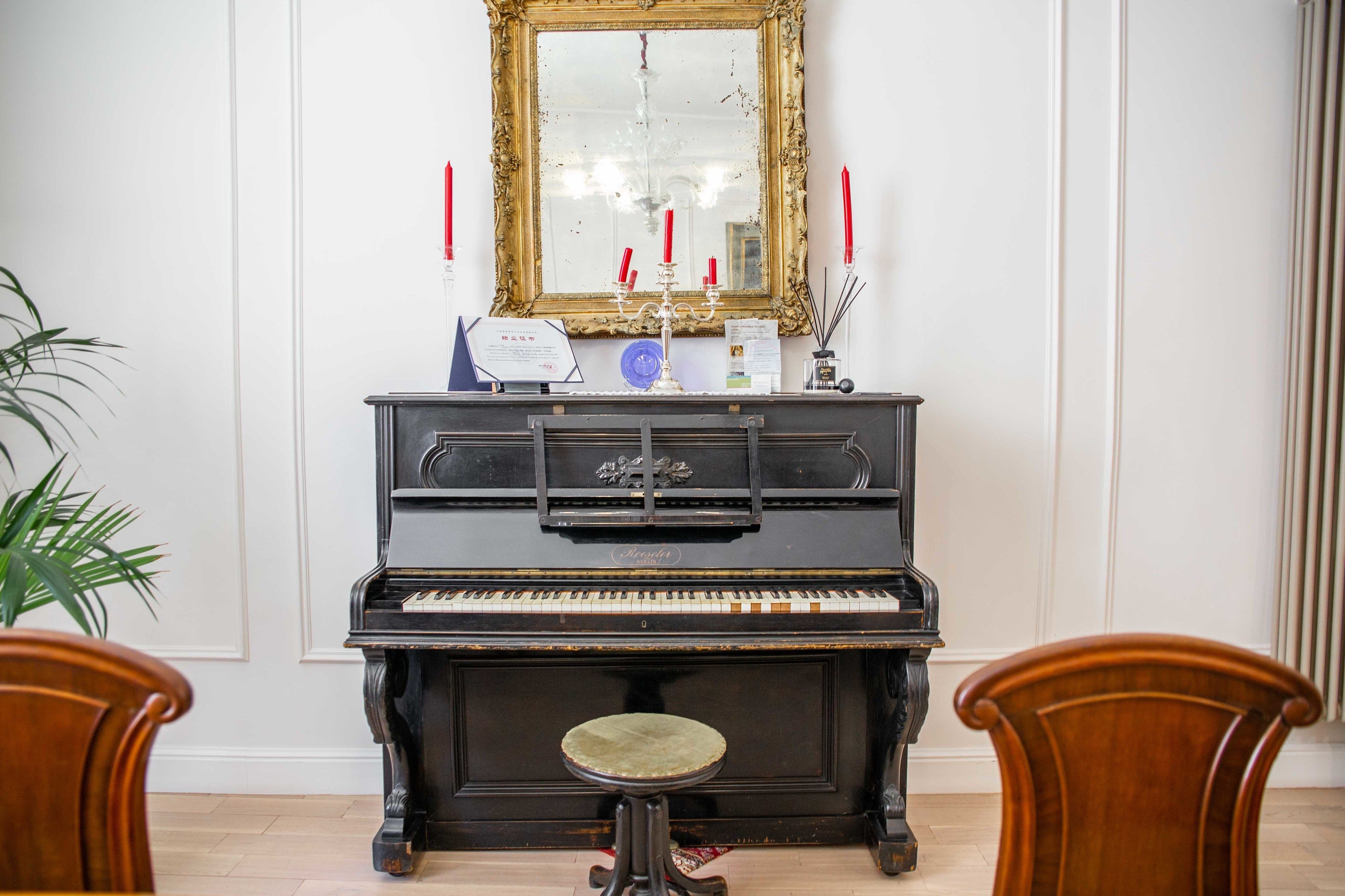 A grand piano with a mirror above it, a candelabra with red candles, and a small stool in front.