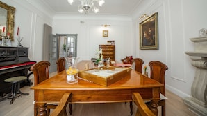 A dining room with a wooden table, chairs, a piano, and a chandelier.
