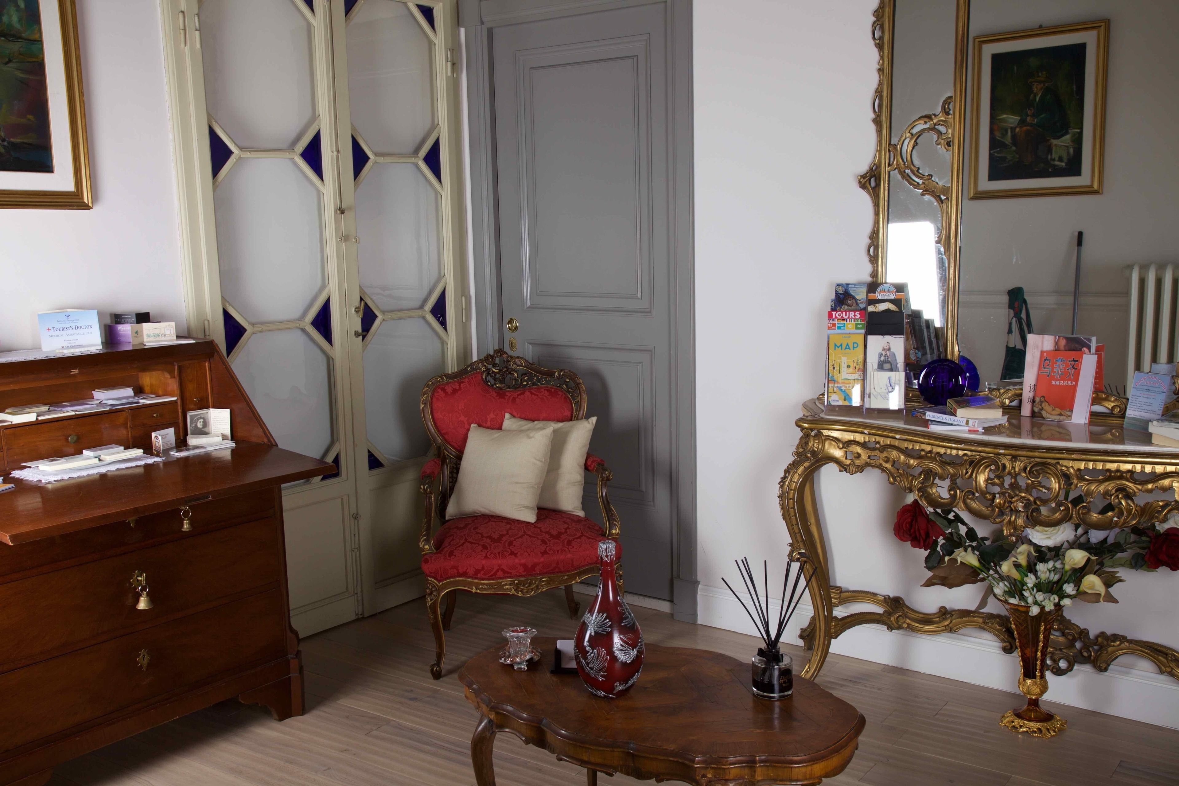 A room with a wooden desk, a red upholstered chair, a gold-framed vanity, and a mirror.