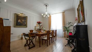 A dining room with a wooden table and chairs, a chandelier, a piano, and a painting on the wall.