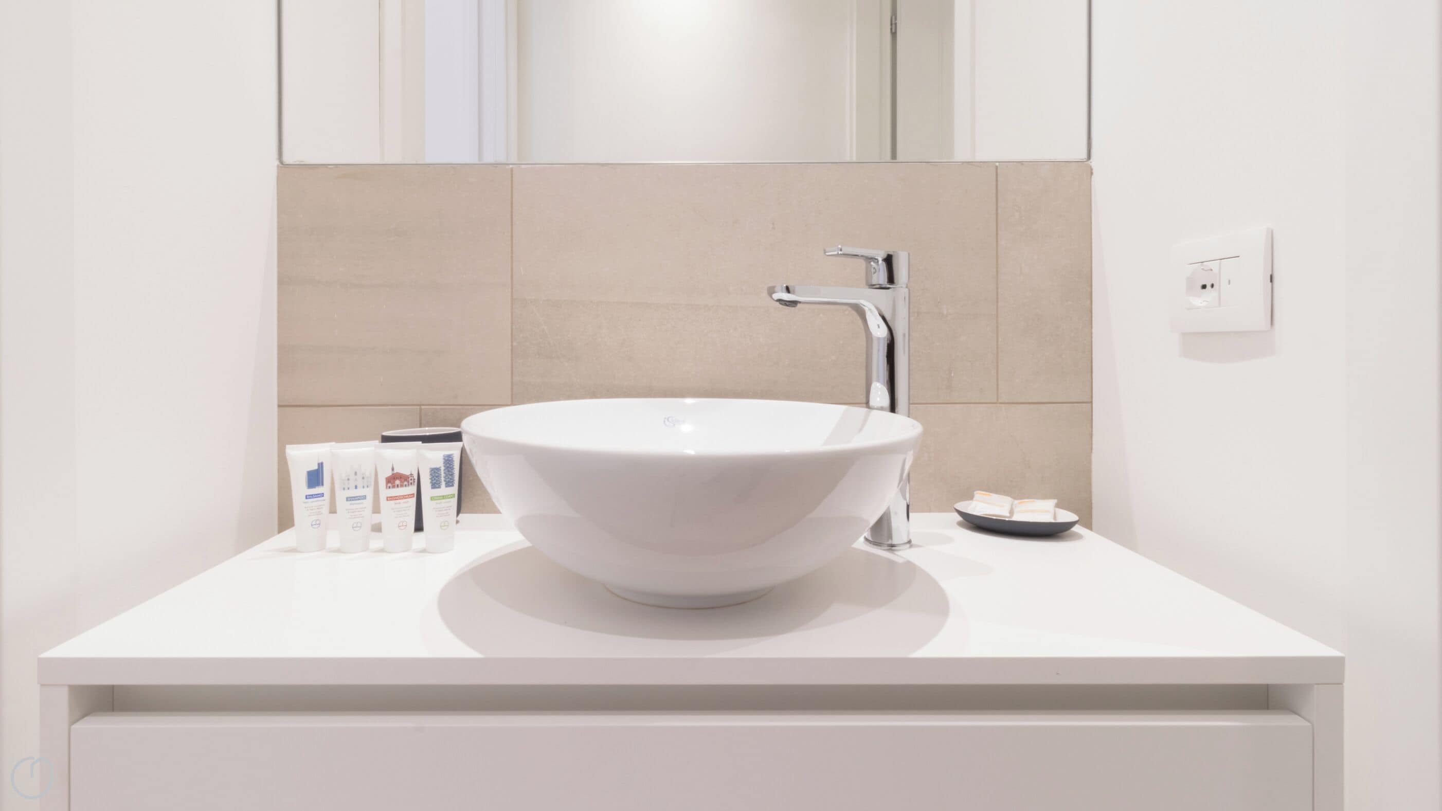 A modern bathroom with a white sink, a mirror, and a beige tiled wall.