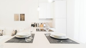 Un espace de salle à manger moderne et minimaliste, avec une table blanche dressée pour deux personnes, deux verres à vin et un couteau posé sur un set de table.