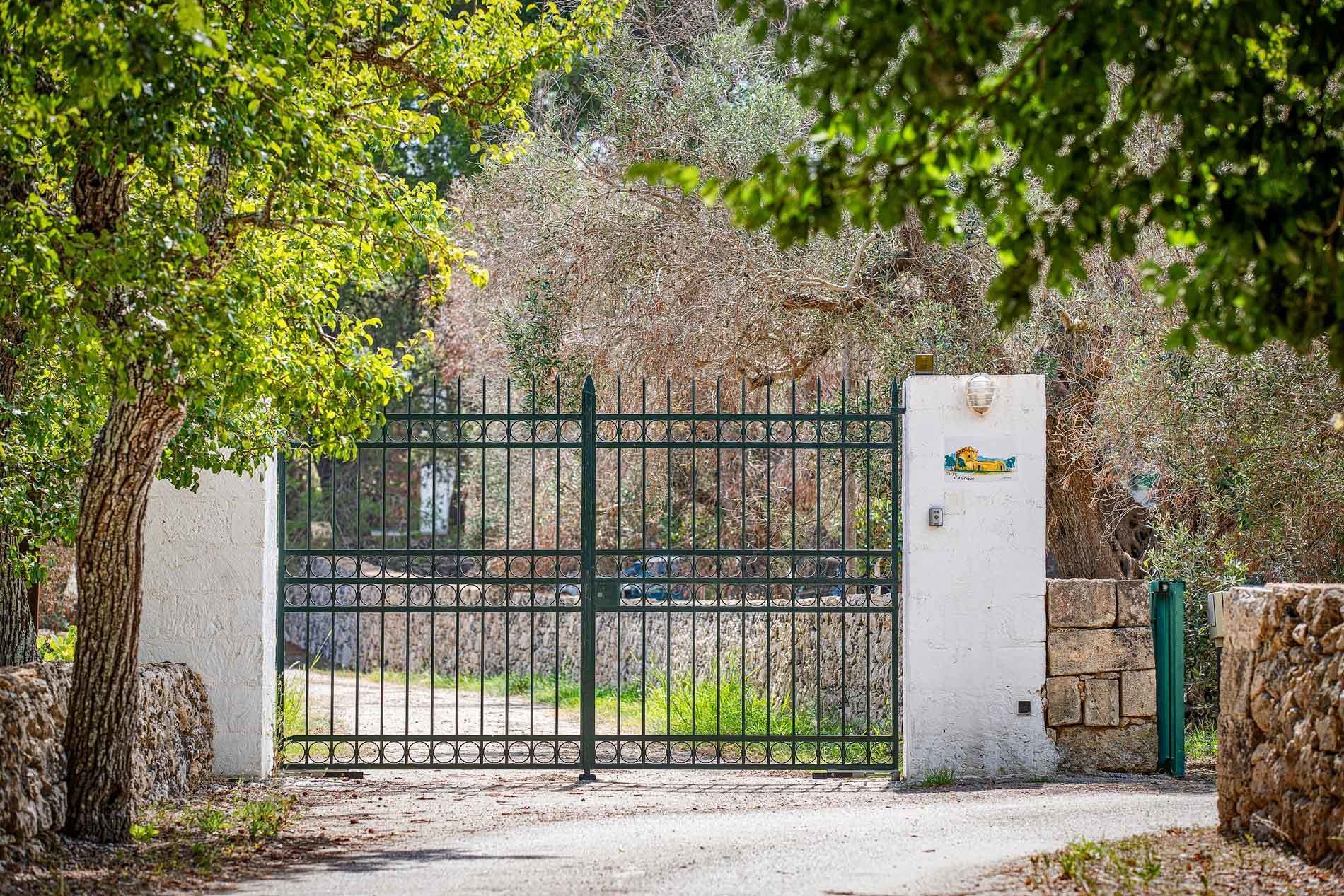 A gated entrance with a metal gate, a white wall, and a stone wall in the background.