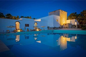 Zona junto a la piscina con vista despejada, un edificio de piedra y otro de blanco con ventanas arqueadas.