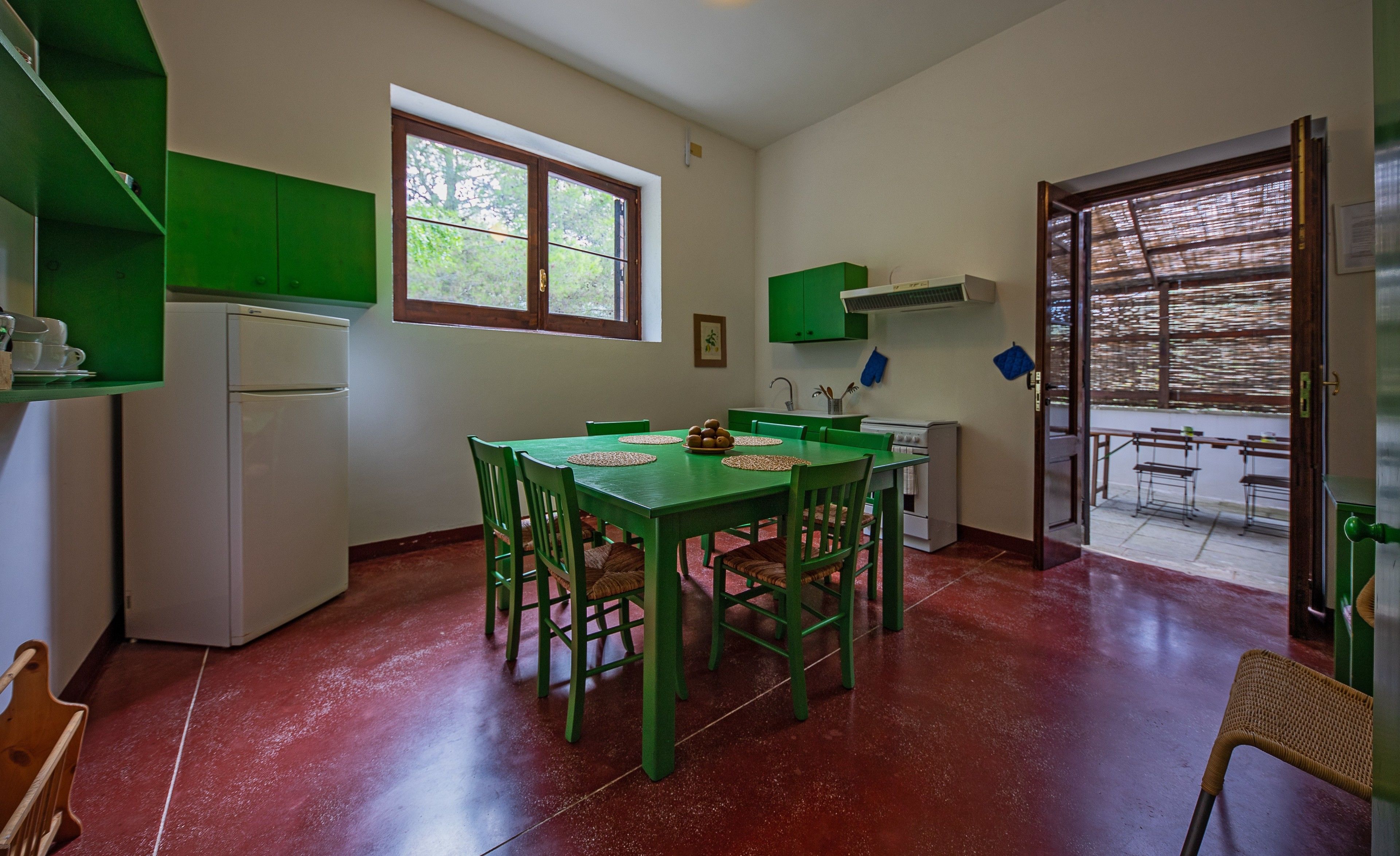 A compact kitchen with green cabinets, a dining table with chairs, a refrigerator, and a window.