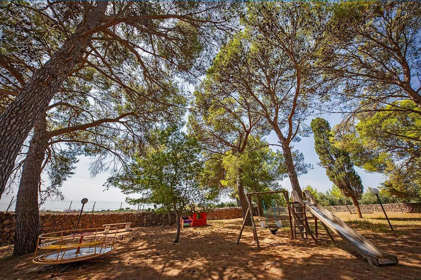 Une aire de jeux avec des balançoires, un toboggan et une structure d’escalade, le tout entouré d’arbres.