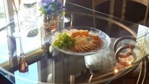 Une table de salle à manger avec un plateau en verre, une assiette de nourriture, un verre de vin et un vase rempli de fleurs.