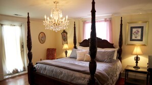 Un lit à baldaquin surmonté d’un lustre, une table de chevet avec une lampe et un tableau encadré accroché au mur.