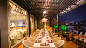Un restaurante con una larga mesa dispuesta para una comida, rodeado de sillas de mimbre, bajo un área techada con ventilador de techo.