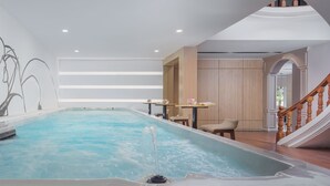 Una amplia piscina interior con un jacuzzi, suelo de madera y una escalera que lleva a un nivel superior.