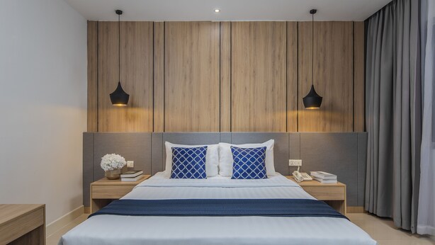 Un dormitorio moderno con cabecera de madera, dos lámparas de noche, un teléfono y una mesita de noche con un florero y libros.