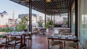 Un área de comedor al aire libre con mesas y sillas, plantas en macetas y vistas a la ciudad.