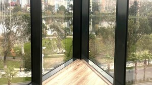 A corner room with large windows, a wooden floor, and a view of a cityscape and park. - Bellevue Residence Suites (Batumi)