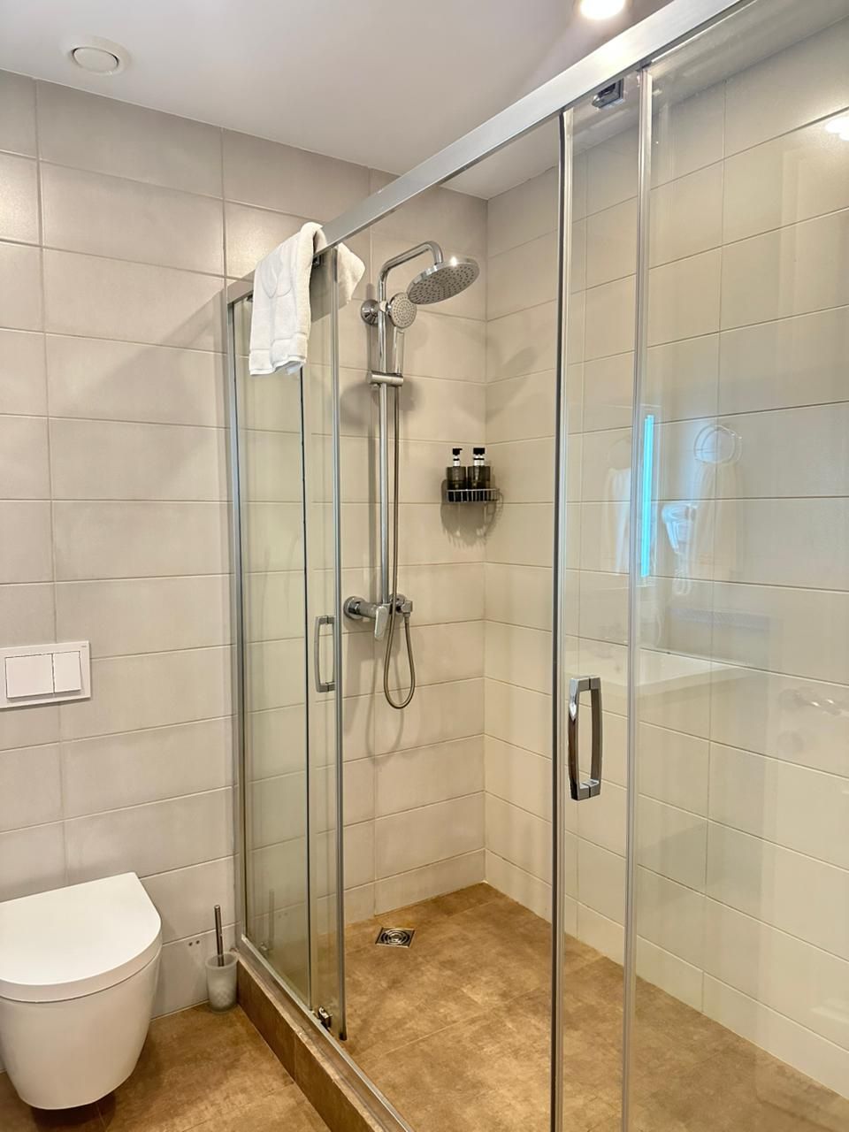 A modern bathroom with a glass-enclosed shower, a white toilet, and a tiled floor.