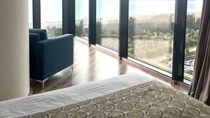 A modern hotel room with large floor-to-ceiling windows, a blue sofa, and a patterned bedspread. - Bellevue Residence Suites (Batumi)