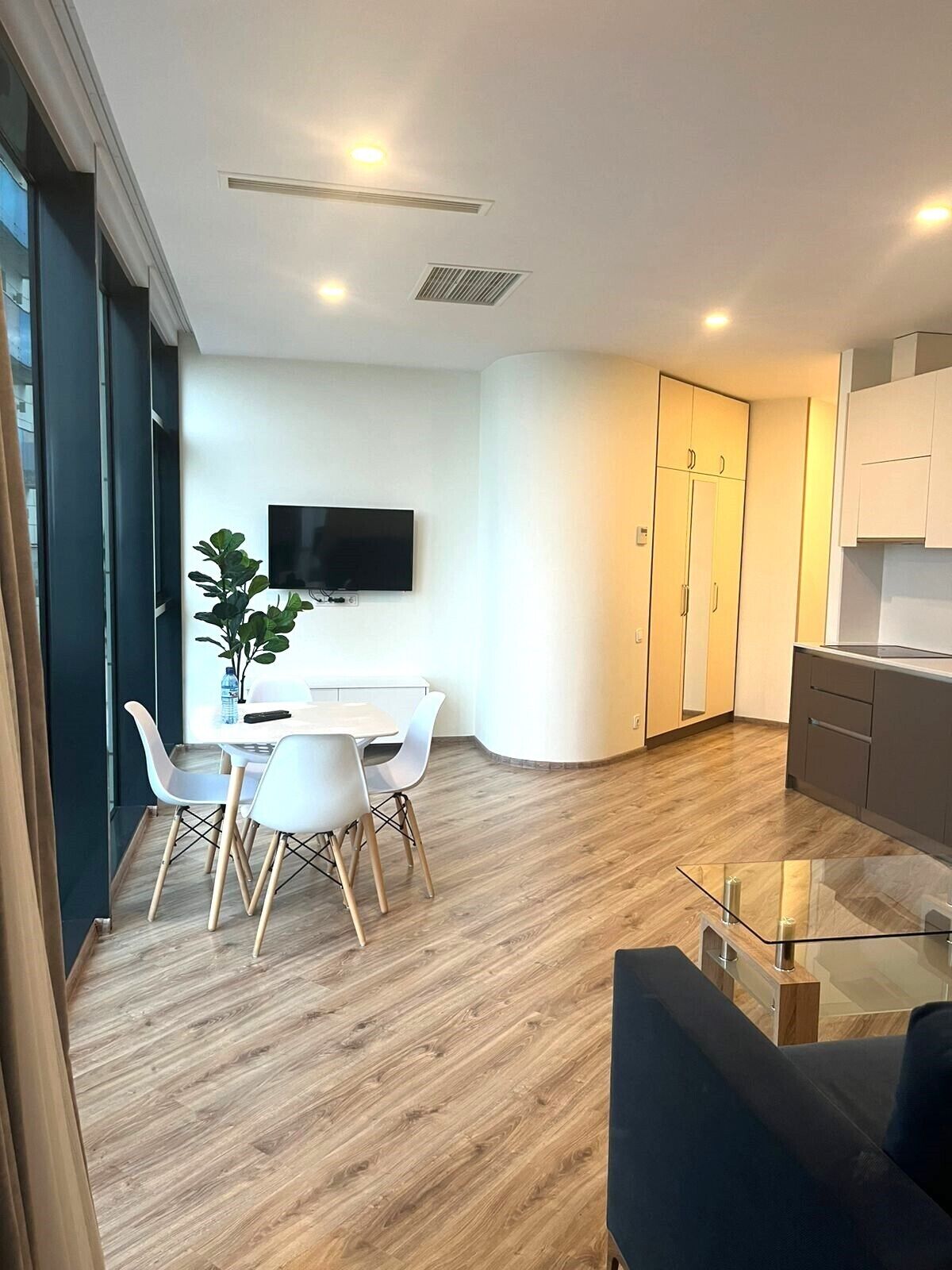 A modern kitchen with white cabinets, a built-in oven, and a flat-screen TV mounted on the wall.