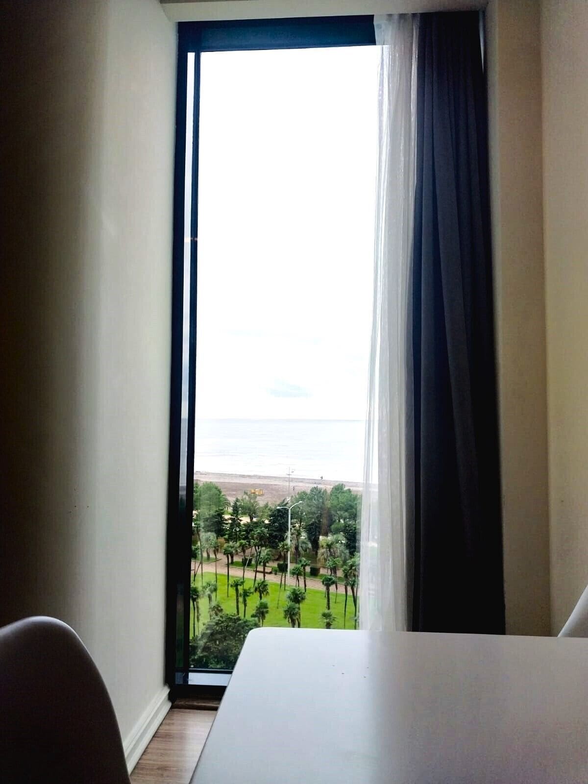 Une chambre dotée d’une grande fenêtre, d’un lit et offrant une vue sur un paysage verdoyant et une plage.